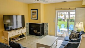Una sala de estar con televisor, sofá, chimenea y vistas al exterior a través de un ventanal corredera.