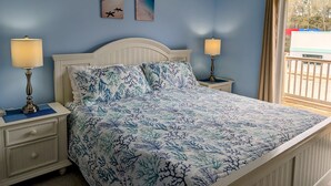Un dormitorio con una cama, dos mesitas de noche, dos lámparas, una ventana con cortinas y dos obras de arte en la pared.