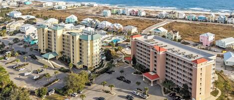 An aerial view of a coastal hotel area with multiple buildings, a parking lot, and a beach in the background.