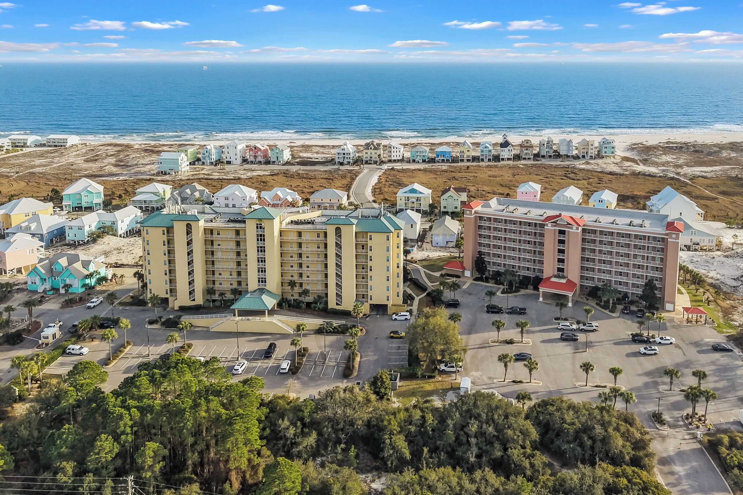 Un complexe hôtelier situé sur la côte, composé de plusieurs bâtiments, doté d’aires de stationnement et offrant une vue sur la plage.
