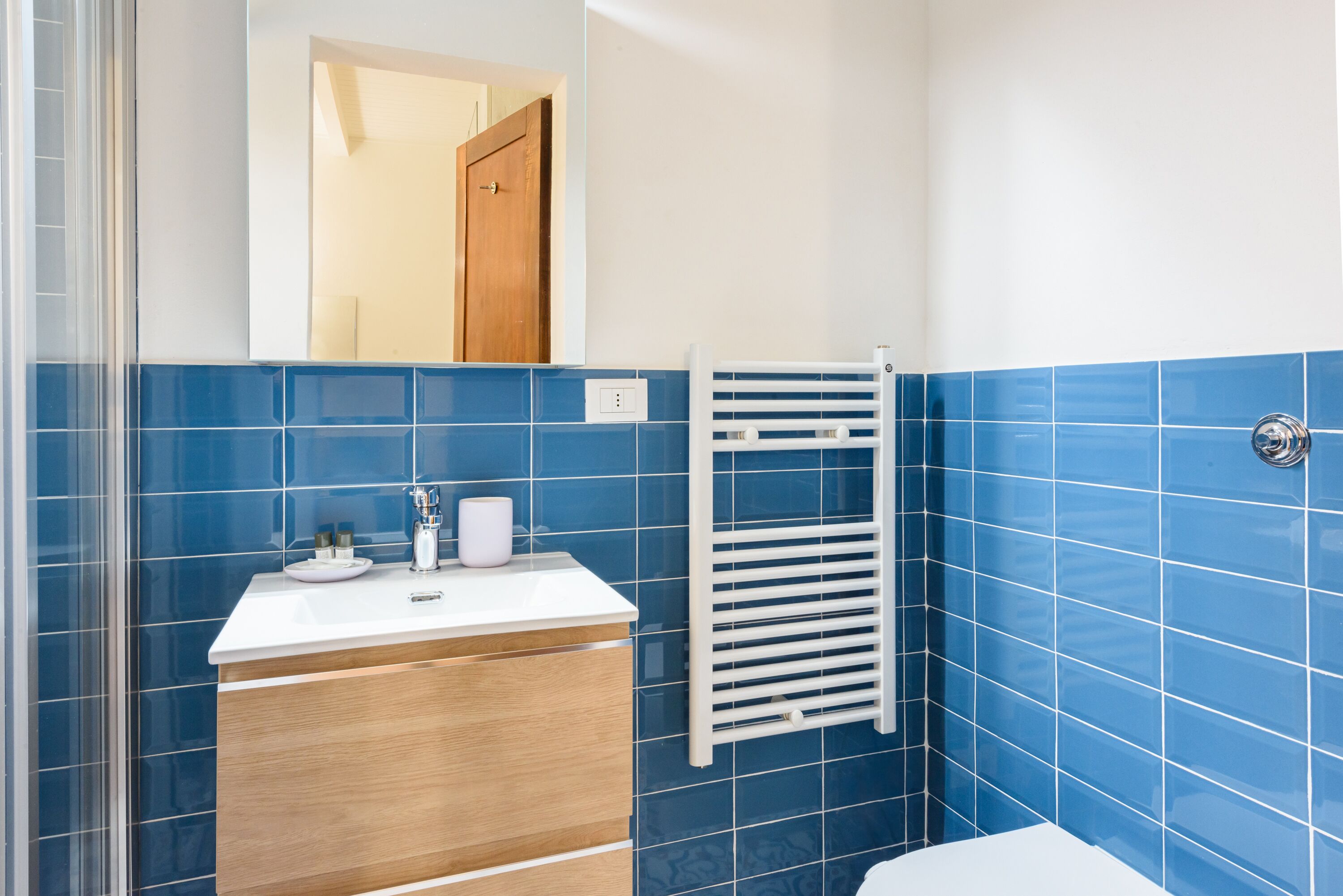 A bathroom with a white sink, wooden cabinet, and a towel rack against blue tiled walls.