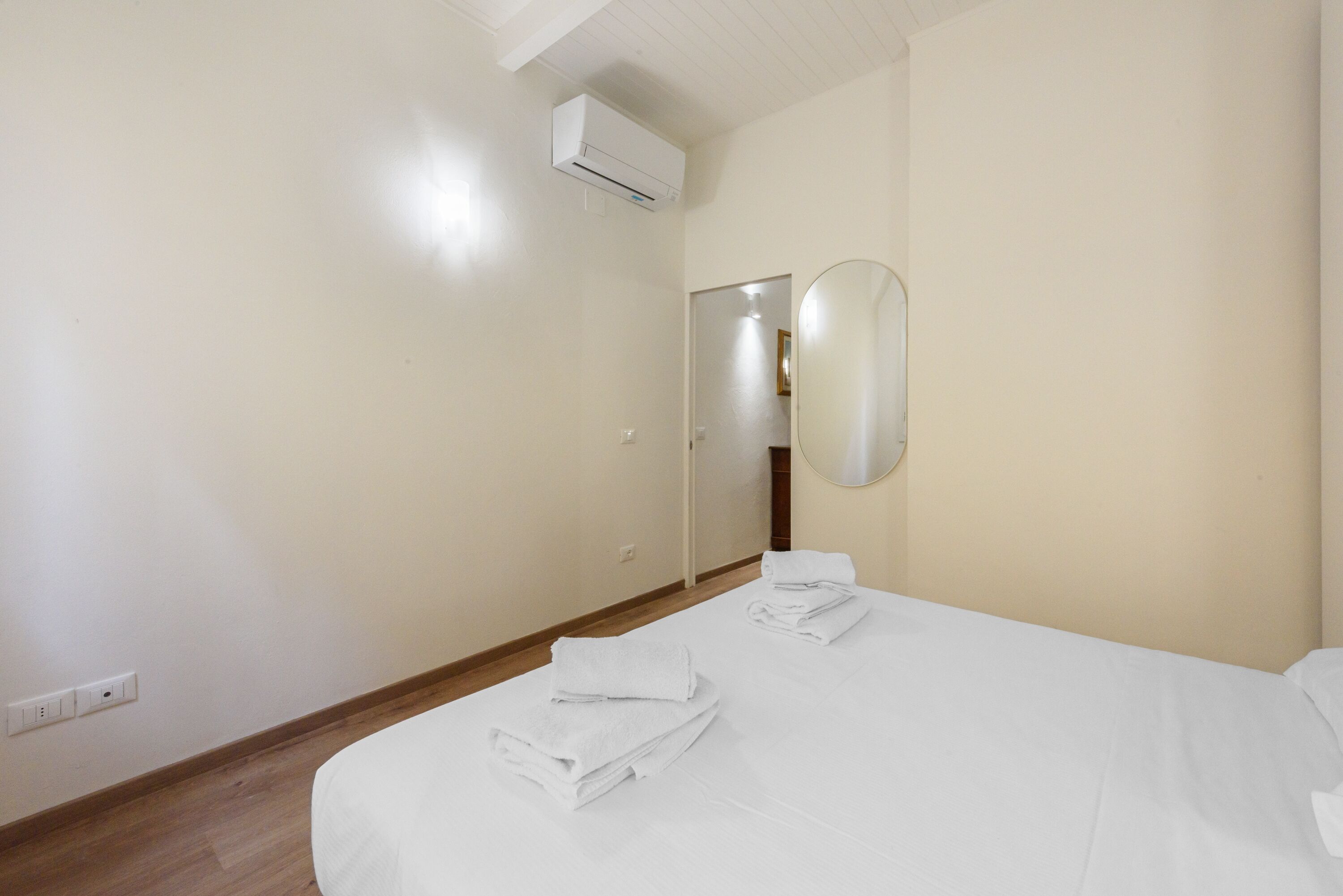 A hotel room with a bed, a mirror, and an air conditioning unit.