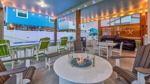 An outdoor seating area with round tables, chairs, and a central fire feature. - Exquisite Beach Retreat You Won't Want To Miss! Pet-Friendly (Port Aransas)