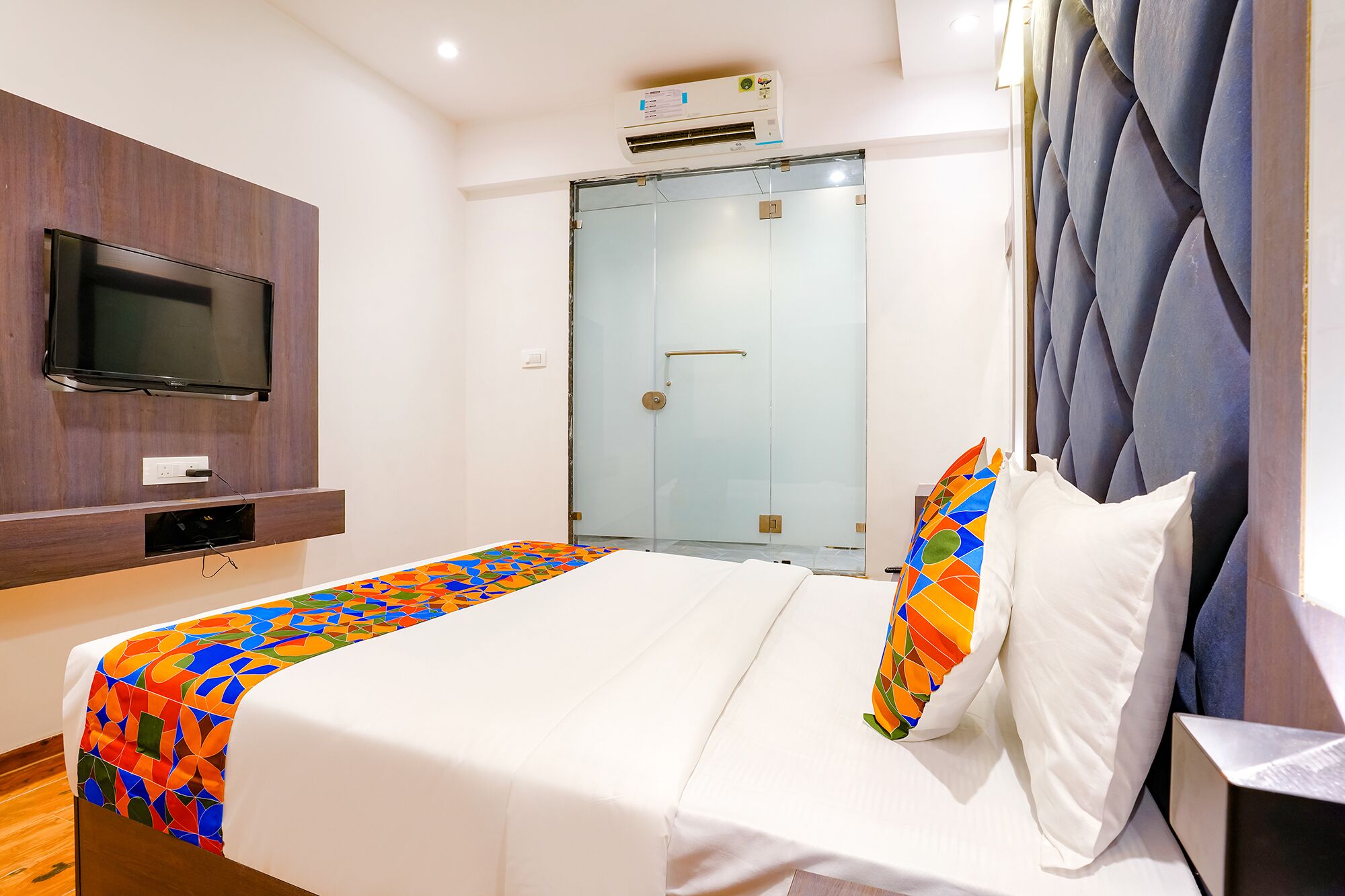 Een hotelkamer met een bed, een aan de muur bevestigde televisie, een deur en een airconditioner.