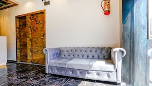 A lobby with a grey tufted sofa, a wooden door with a number, and a fire extinguisher on the wall. - Hotel Gorrion (Mumbai)
