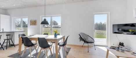 A modern kitchen with a dining area, large windows, and a TV mounted on the wall.
