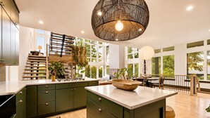 Une cuisine moderne avec des meubles de couleur verte, un grand îlot central et un luminaire suspendu.