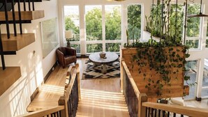 Un intérieur moderne avec un escalier en bois, une table ronde et une grande fenêtre donnant sur un paysage verdoyant.