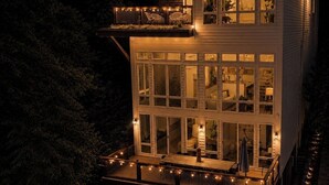 Une maison moderne à deux étages, dotée de grandes fenêtres, d’un balcon et d’un éclairage extérieur.