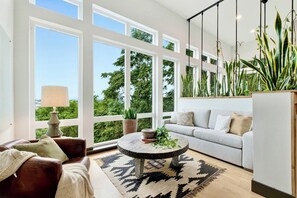 A modern living room with large windows, a round coffee table, a sofa, and a potted plant.