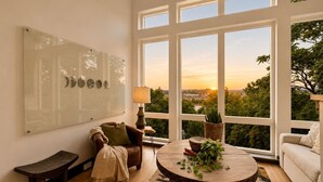 Une pièce spacieuse avec de grandes fenêtres, une table basse ronde en bois, un fauteuil en cuir et un canapé blanc.