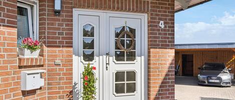 A brick house with a white double door, a garage door, and a potted plant in front.