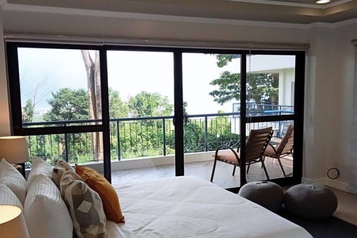 A bedroom with a large bed, a balcony with chairs, and a view of greenery.