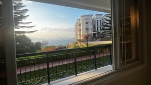 A view from a window with a metal railing, overlooking a street with buildings and a clear sky. - Trillo Bay Villas (Morong)