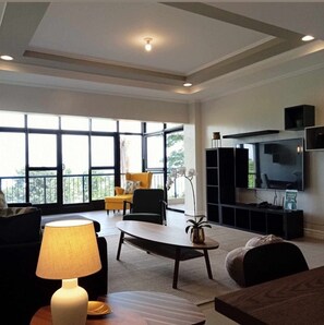 A spacious living room with a large TV, comfortable seating, and a balcony view. - Trillo Bay Villas (Morong)