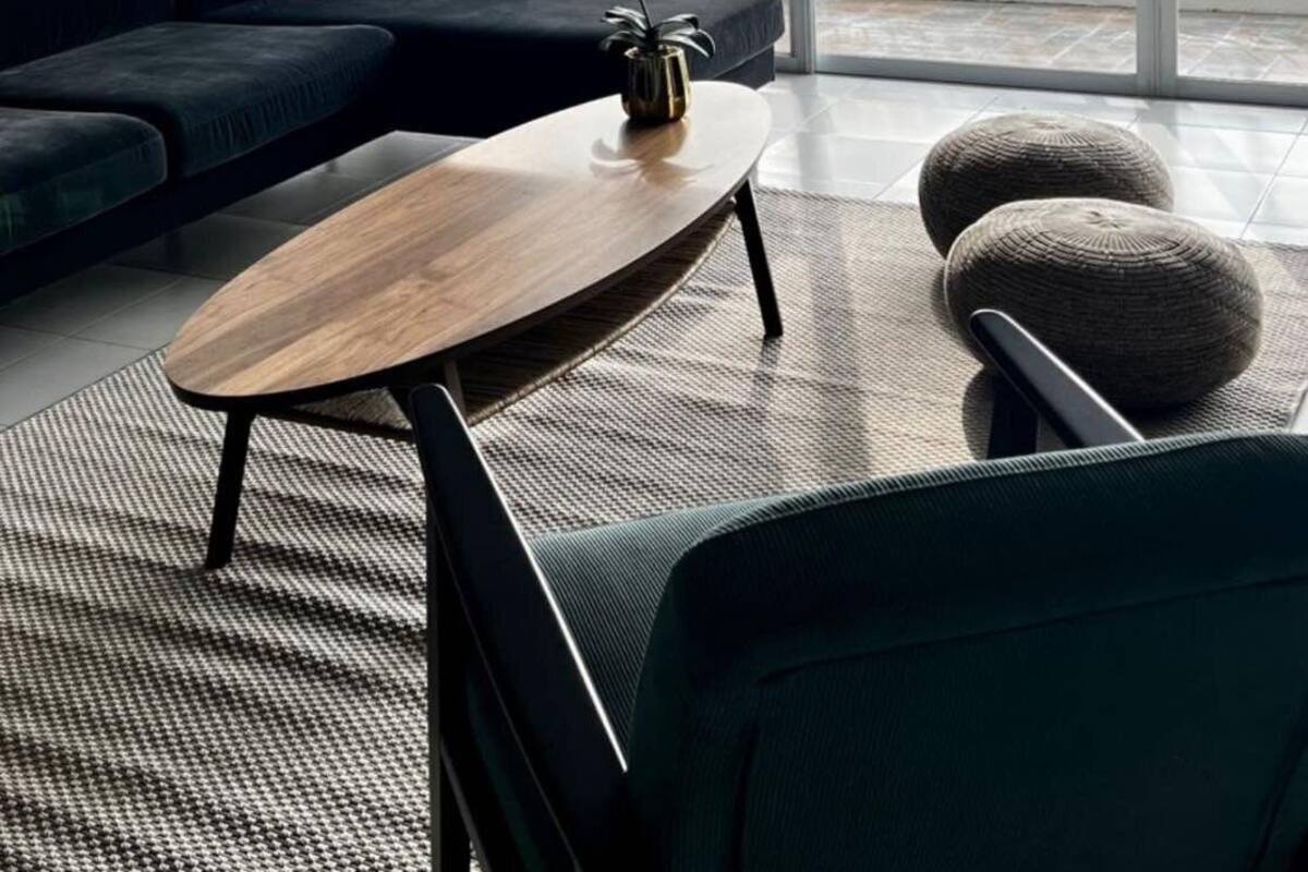 A modern living room with a dark sofa, a wooden coffee table, and a view of a balcony with greenery.