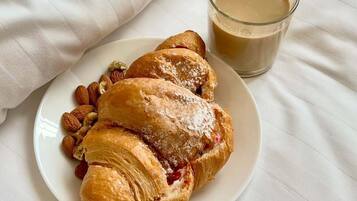 Um prato com um croissant e amêndoas, e um copo de café sobre um lençol branco.