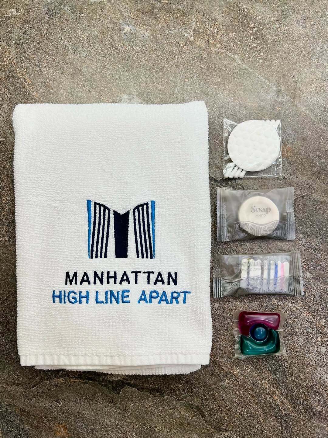 Una toalla con el bordado 'Manhattan High Line Apart', una pastilla de jabón, un cepillo de dientes y una pequeña botella de champú.