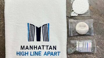 Una toalla con el bordado 'Manhattan High Line Apart', una pastilla de jabón, un cepillo de dientes y una pequeña botella de champú.