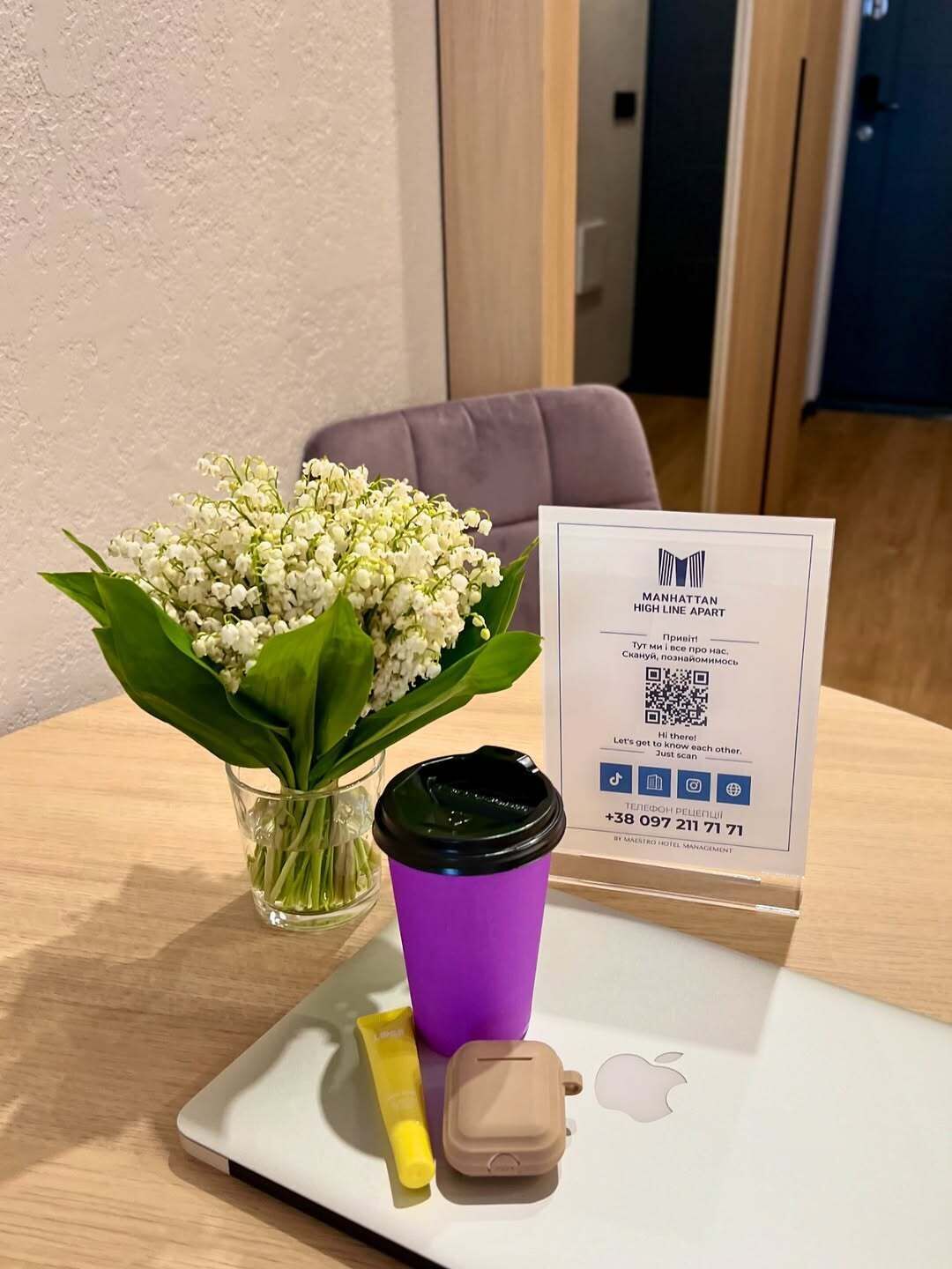 Un ordinateur portable avec une tasse violette, une petite bouteille et un récipient posés sur son écran, ainsi qu'un code QR et du texte sur un support.