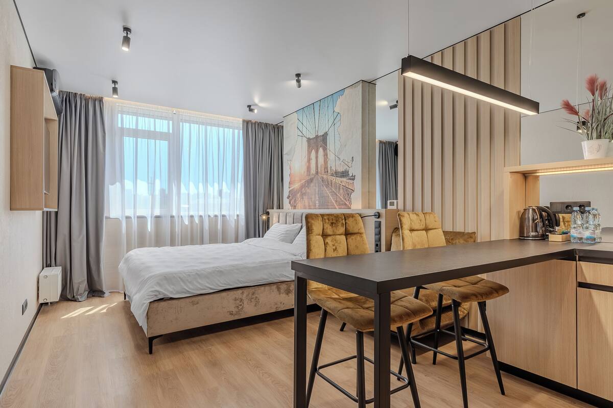 Ein modernes Hotelzimmer mit Bett, Schreibtisch und Stuhl. Es gibt ein Fenster mit Vorhängen, ein Bild an der Wand und eine Pflanze auf dem Schreibtisch.