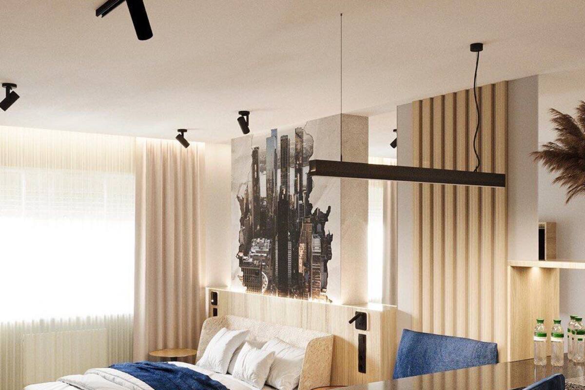 Ein modernes Hotelzimmer mit einem Bett, einem Esstisch mit zwei Stühlen, einem Stadtbildgemälde an der Wand und einem großen Fenster mit Vorhängen.