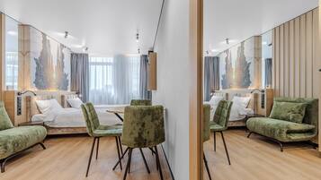 A modern hotel room with a large mirror reflecting the room's interior, a bed with white linens, green upholstered chairs, and a wooden floor.