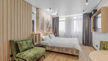 A modern hotel room with a bed, a green armchair, a small table, and a large mirror.