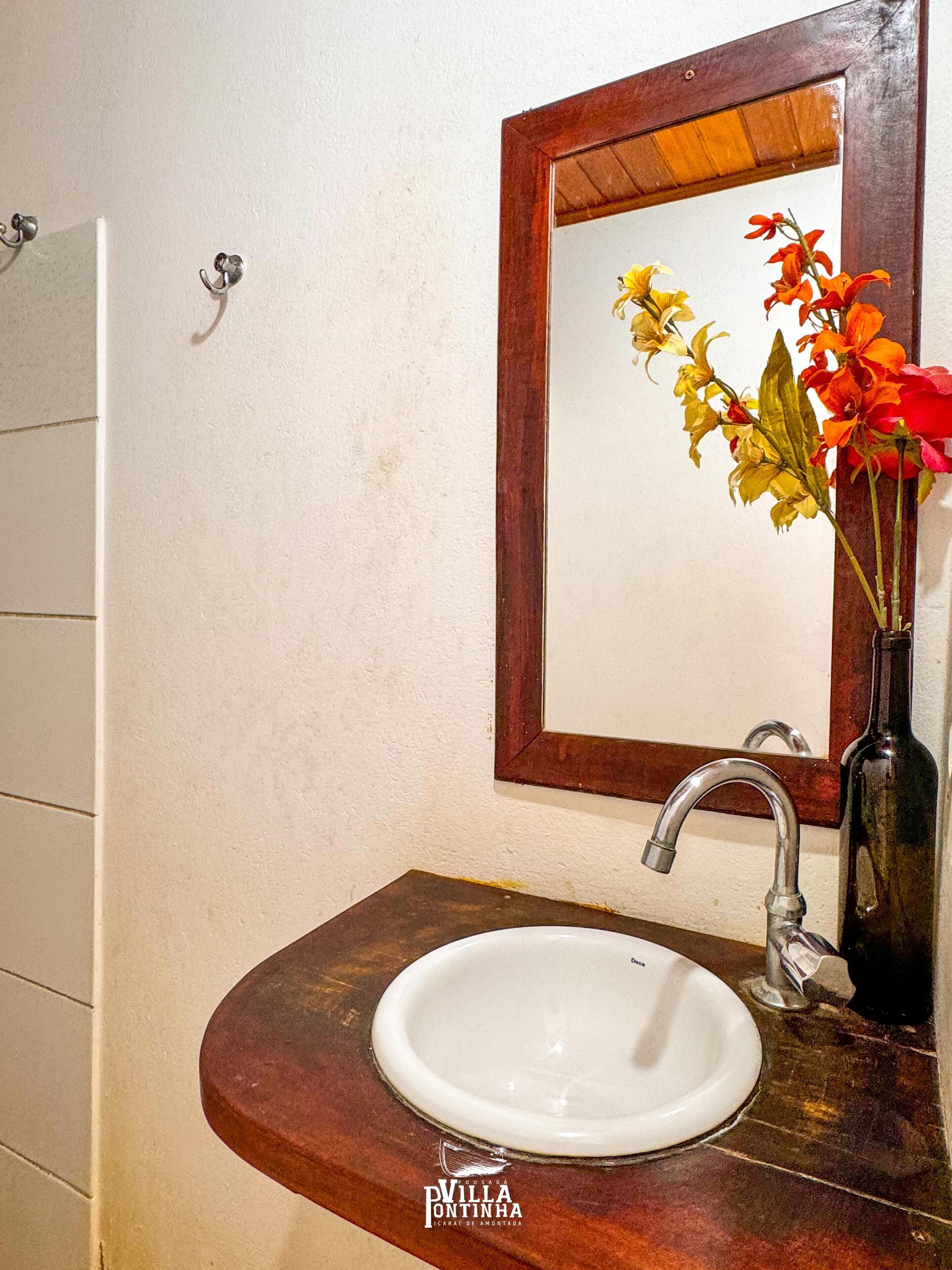 Ein Badezimmer mit einem weißen Waschbecken, einer Holzkommode, einem Spiegel und einer Vase mit Blumen.