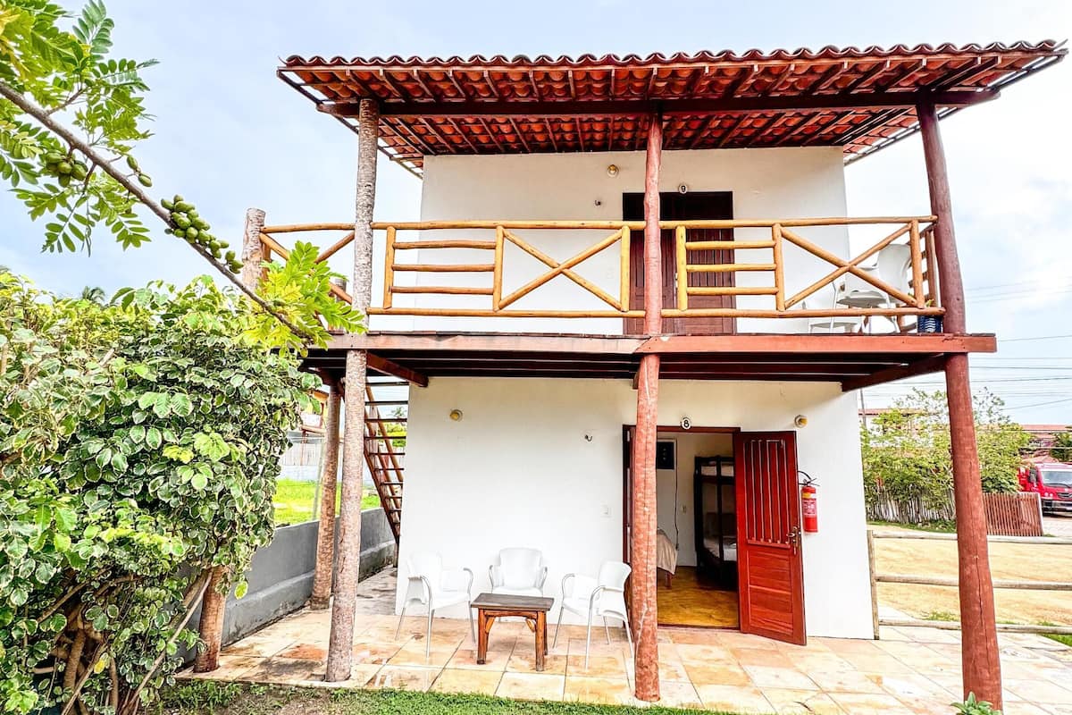 A two-story building with a balcony, a wooden table, and chairs outside.