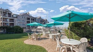 A patio area with outdoor seating and umbrellas, a grassy lawn, and a building with multiple balconies in the background. - Harborfront Charm at Wyndham Onshore Resort (Newport)