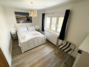A bedroom with a bed, a window, a radiator, a nightstand, and a chair. - Coach House Annexe (Sandown)