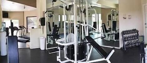 Ein Fitnessstudio mit verschiedenen Trainingsgeräten, darunter ein Squat-Gestell, Bänke und Kurzhanteln.