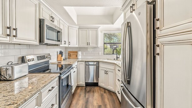 A modern kitchen with white cabinetry, stainless steel appliances, and a granite countertop. - Exceptional upgrades makes for a perfect short or long term stay (TUCSON)