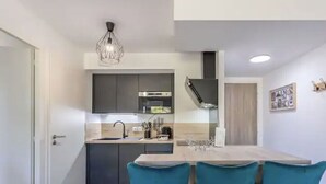 A modern kitchen with dark cabinets, a built-in oven, and a large island with bar stools. - Le cosy de Duingt, charmant appartement à 150m du lac (Duingt)