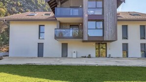 A modern two-story building with a balcony on the upper floor, a flat roof, and a mountain backdrop. - Le cosy de Duingt, charmant appartement à 150m du lac (Duingt)