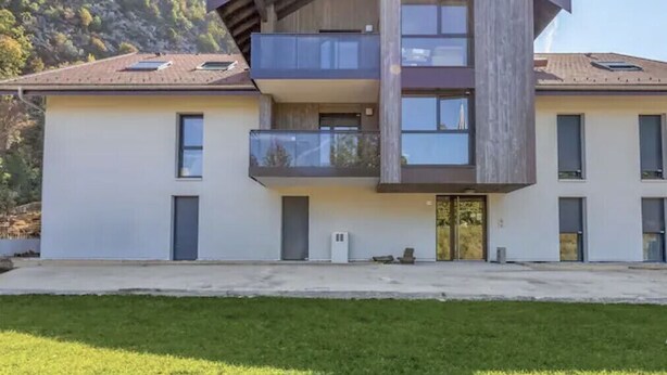 A modern two-story building with a balcony on the upper floor, a flat roof, and a mountain backdrop. - Le cosy de Duingt, charmant appartement à 150m du lac (Duingt)