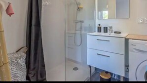 A modern bathroom with a glass shower enclosure, a white vanity with a mirror, and a washing machine. - Le cosy de Duingt, charmant appartement à 150m du lac (Duingt)