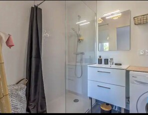 Et moderne badeværelse med en glasbrusekabine, et hvidt vaskemøbel med et spejl, og en vaskemaskine.