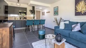 A modern living room with a blue sofa, a coffee table, and a kitchen area in the background. - Le cosy de Duingt, charmant appartement à 150m du lac (Duingt)