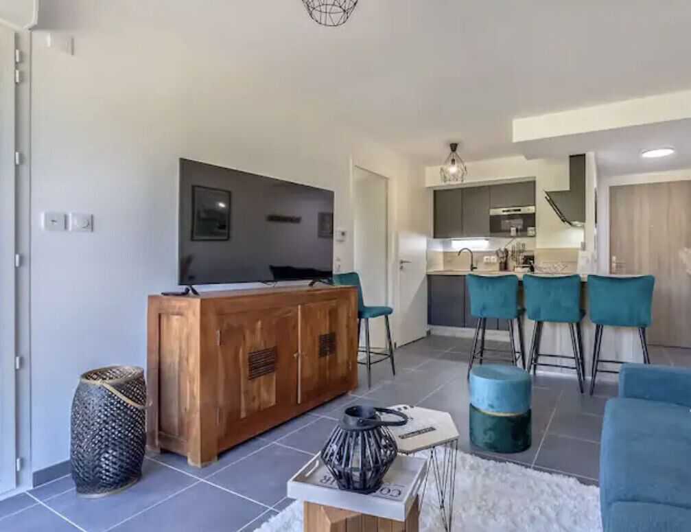 Un espacio habitable moderno con una isla central de madera, taburetes de bar y una cocina al fondo.