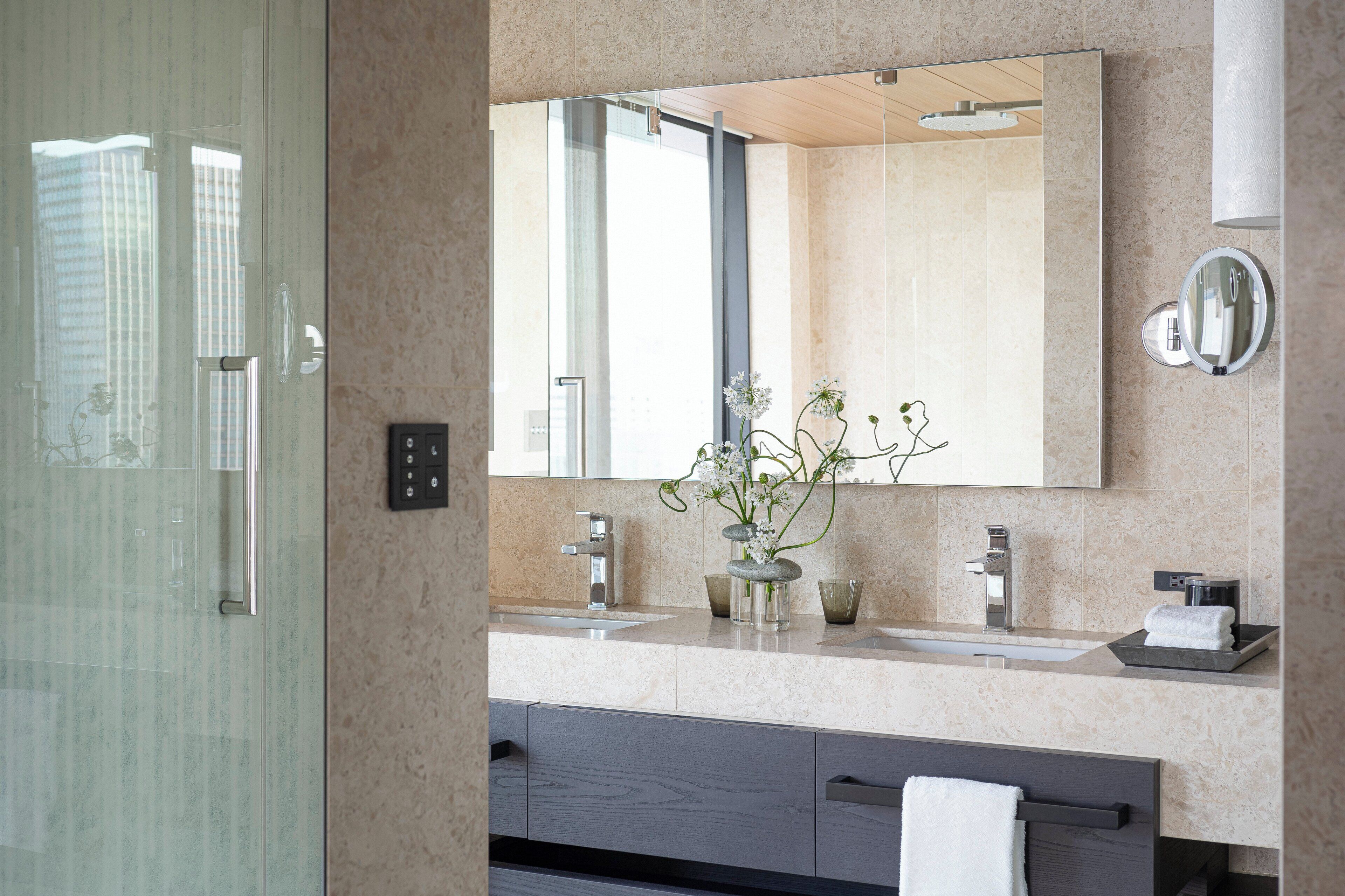 A modern bathroom with a large mirror, two sinks, a towel rack, and a glass shower enclosure.