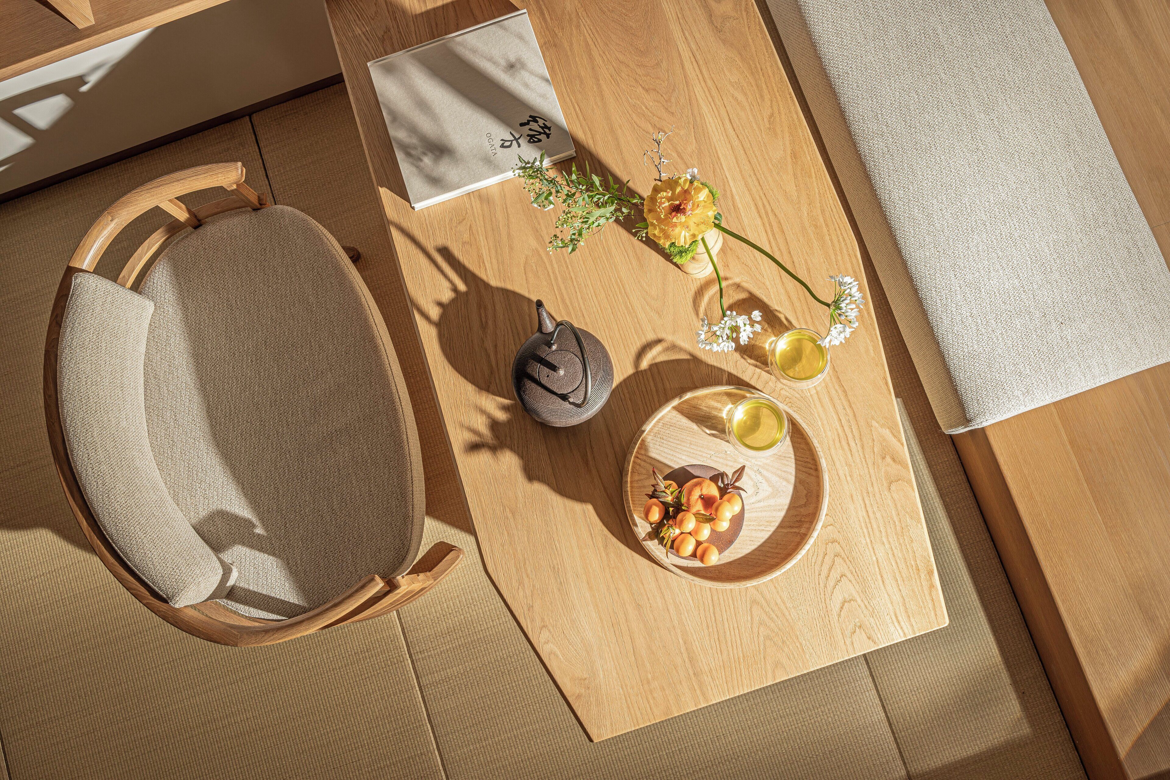A wooden table with a chair, a teapot, a plate with fruit, and a small vase with flowers.