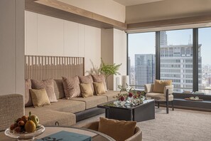 A modern living room with a sofa, armchairs, a coffee table, and a large window with a city view.