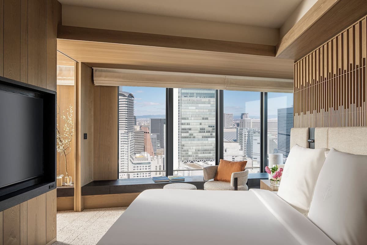Een moderne hotelkamer met een groot bed, een televisie en uitzicht op de stad door grote ramen.