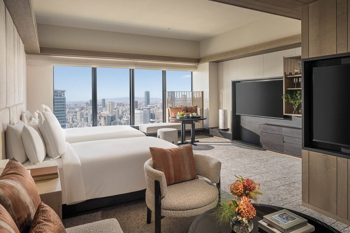 Een moderne hotelkamer met een groot bed, een zithoek met een koffietafeltje, een flatscreen televisie en uitzicht over de stad.