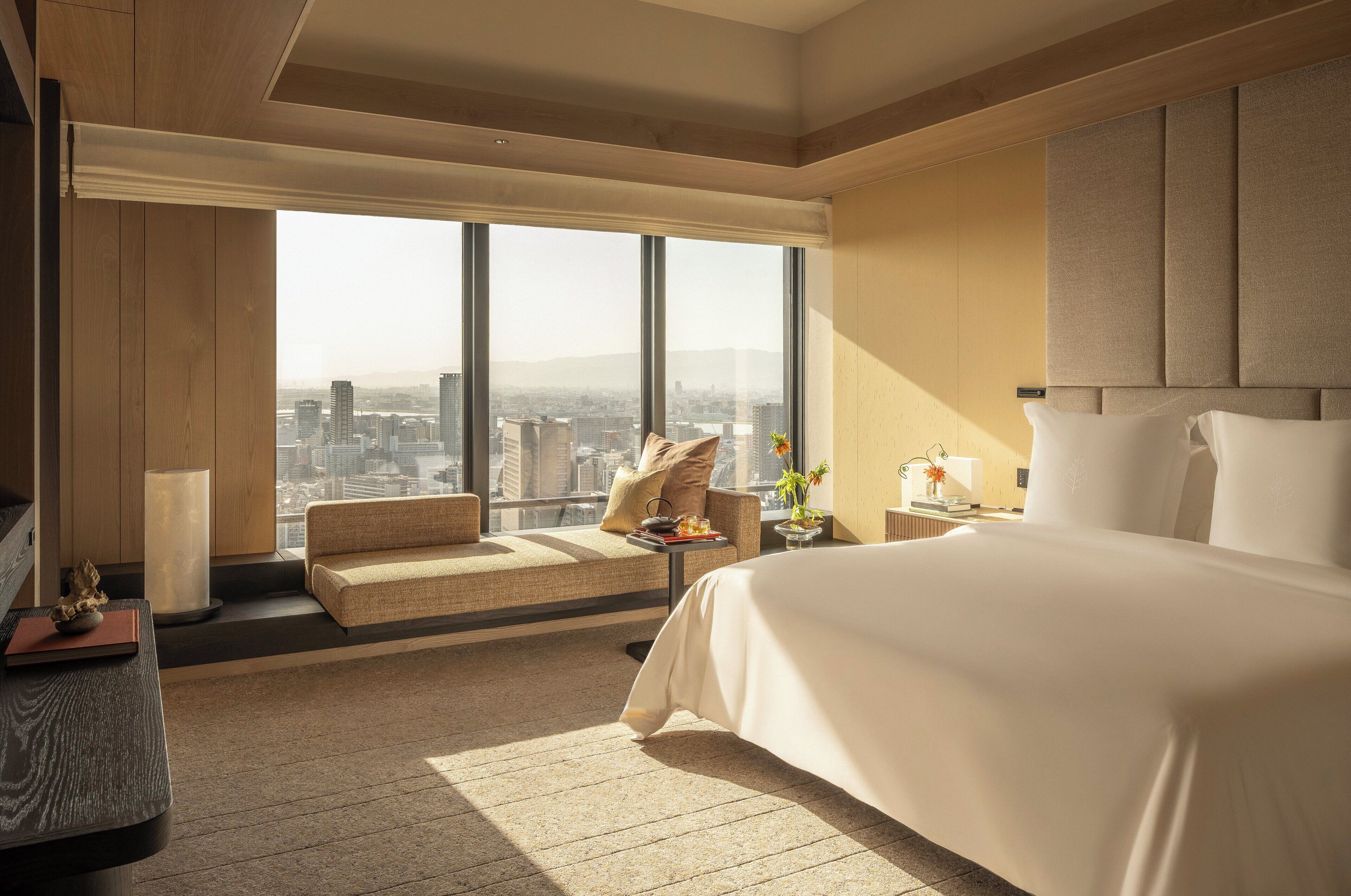 Une chambre d’hôtel moderne dotée d’un grand lit, d’un coin salon avec vue sur la ville et d’une grande fenêtre.
