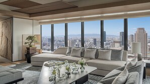 A modern living room with a large sofa, a coffee table with decorative items, and a city view through large windows. - Four Seasons Hotel Osaka (Osaka)