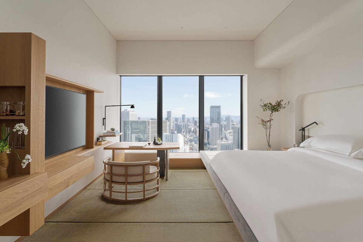 Een moderne hotelkamer met een groot bed, een bureau, een televisie en uitzicht op de stad.