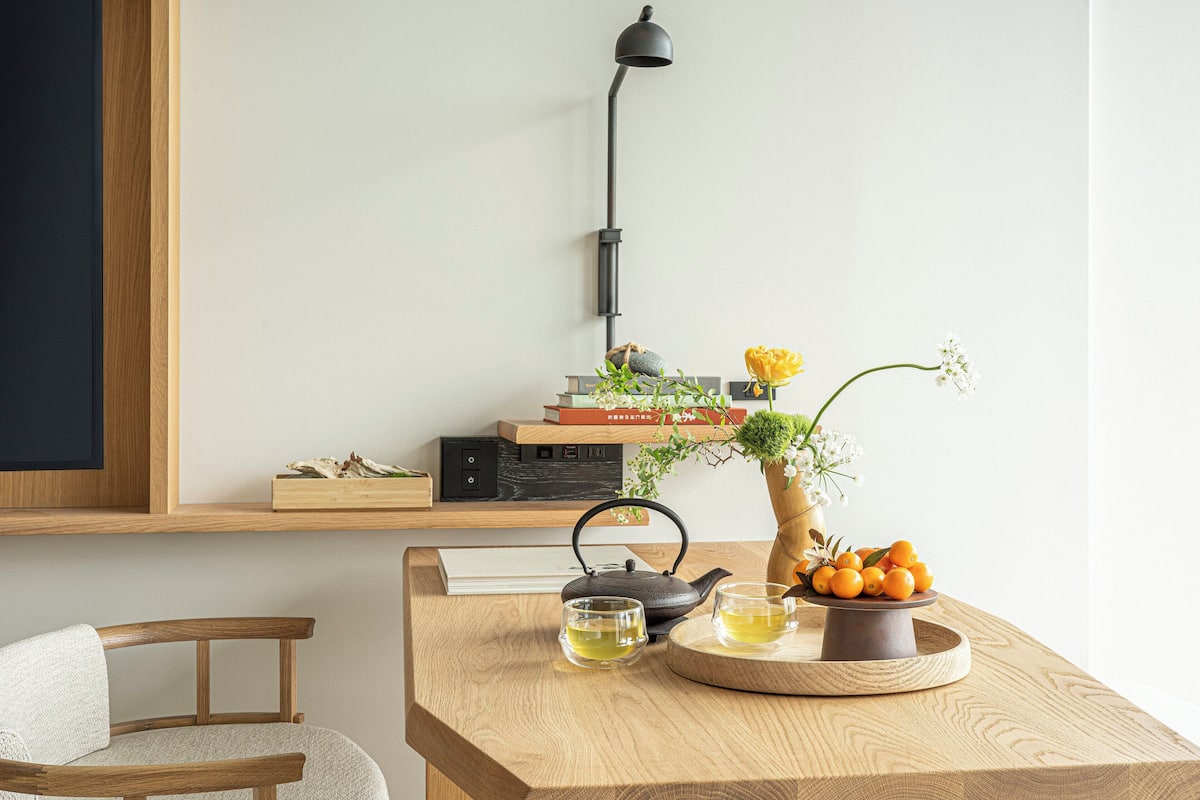 Een houten tafel met een waterkoker, theekoppen en een schaal oranjes.